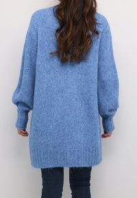 Světle modrý oversized svetr vyrobený z měkkého, texturovaného úpletu. Obsahuje žebrovaný lem a manžety, s delší zadní částí a volnými rukávy.