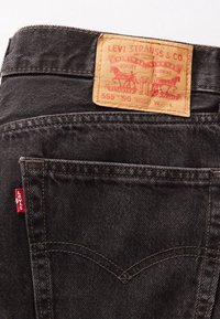 Poche arrière d'un jean en denim noir avec une étiquette en cuir Levi Strauss & Co. et une petite étiquette en tissu rouge Levi's sur la couture latérale.