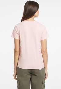 Jasnoróżowa koszulka z krótkim rękawem o klasycznym okrągłym dekolcie, wykonana z miękkiej bawełny. Ma prosty krój i zestawiona jest z oliwkowymi spodniami typu cargo.