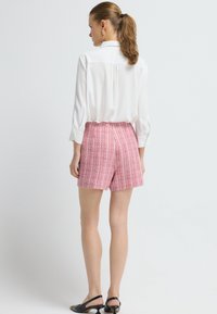 Bílá košile s knoflíky, růžové vzorované šortky, moderní střih, texturovaná tkanina a černé lodičky na podpatku s malým podpatkem.