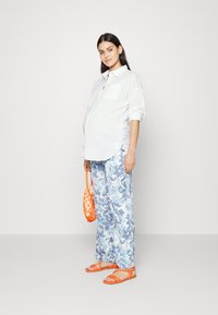 Camisa branca de botões, calças florais em azul claro, saco texturizado laranja e sandálias planas laranjas. Design simples e de ajuste relaxado.