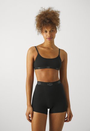 Bralette nera con spalline sottili e banda con logo; pantaloni corti neri a vita alta abbinati con cintura con logo. Texture liscia, design minimalista.