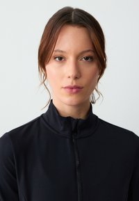 Giacca nera zip-up con colletto alto, realizzata in tessuto liscio e elasticizzato. Design minimalista senza abbellimenti visibili.