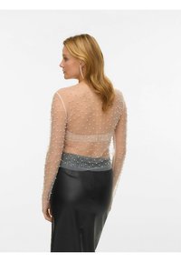 Transparent genser med lange ermer, perlepynt, nude materiale og et grått satengbelte, kombinert med et svart skinnskjørt.