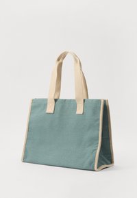 Canvas tote bag i teal med beige håndtak og kant. Strukturert, rektangulær form med forsterkede sømmer. Lett og slitesterkt materiale.