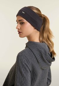 Un bandeau en tricot gris avec une texture nervurée et un accent métallique, associé à un sweat à capuche gris texturé avec un grand col et une fermeture éclair.