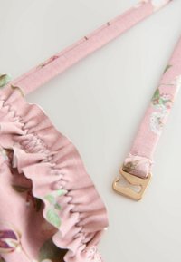 Sangle en tissu à fleurs roses avec une fermoir en crochet doré attaché à un bord de tissu froncé sur un fond clair.