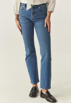 Blaue Jeans aus Denim mit geradem Bein, sauberem Design, dezentem Verblassen, kontrastierenden Nähten und hoher Taille. Dazu schwarze Loafer kombiniert.