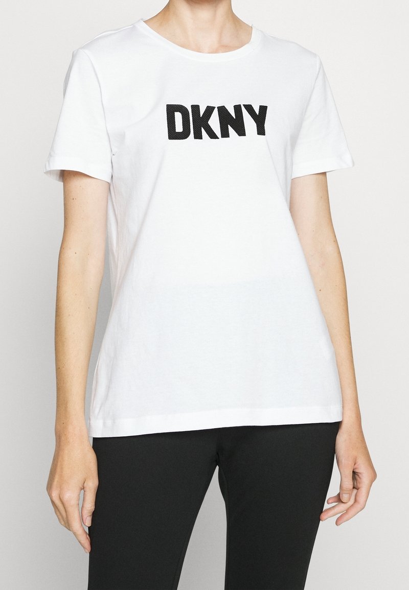 Vit bomulls T-shirt med en stor svart "DKNY" logotyp på bröstet, korta ärmar och klassisk rundad halsringning.