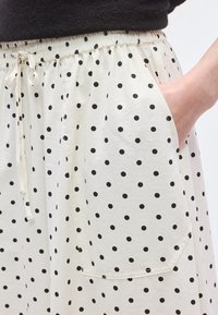 Λευκά σορτς από ύφασμα με μαύρες πουά βούλες, διαθέτουν ελαστική μέση και κορδόνι. Περιλαμβάνουν πλαϊνές τσέπες και είναι με ομαλή υφή.