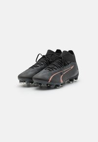 Scarpe da calcio nere con tomaia testurizzata, design mid-top e dettagli rosa. Presentano una chiusura con lacci e tacchetti in gomma per una migliore trazione.