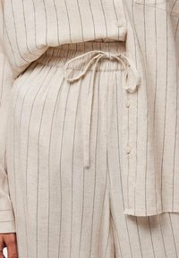 Ensemble en lin composé de deux pièces comprenant un haut fluide avec des boutons et un pantalon à taille élastique, le tout en beige avec de légères rayures noires.
