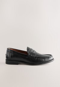 Mocassin pour homme en cuir noir avec couture moc toe, détail de bride penny et petit talon, sur un fond clair uni.