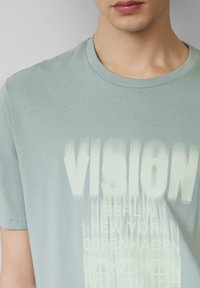 Lichtblauw T-shirt met korte mouwen van zacht materiaal, voorzien van opvallende witte grafische tekst met stadsnamen en een geometrisch patroon.