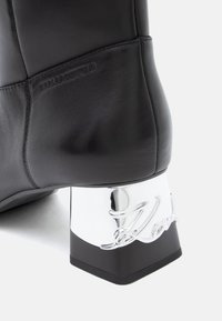 Must mustaöö pedikaga, millel on ristküliku kuju, särava hõbedase plokknõela, millel on graveering ja siledad tekstuuri detailid.