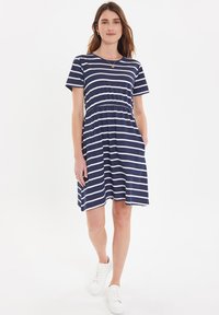 Marineblauwe gestreepte jurk met korte mouwen, elastische tailleband en zijzakken, gecombineerd met witte sneakers. Katoenen materiaal.