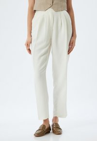 Pantaloni bianchi sartoriali con pieghe, realizzati in un tessuto liscio. Caratterizzati da una gamba dritta e abbinati a mocassini marroni.