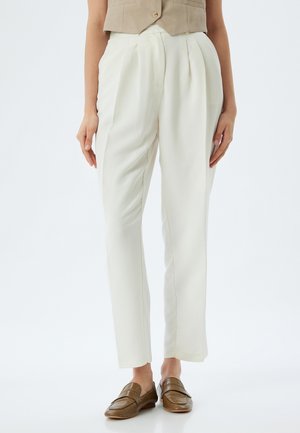 Pantalones blancos ajustados con pliegues, hechos de un tejido suave. Presentan una pierna recta y se combinan con mocasines marrones.