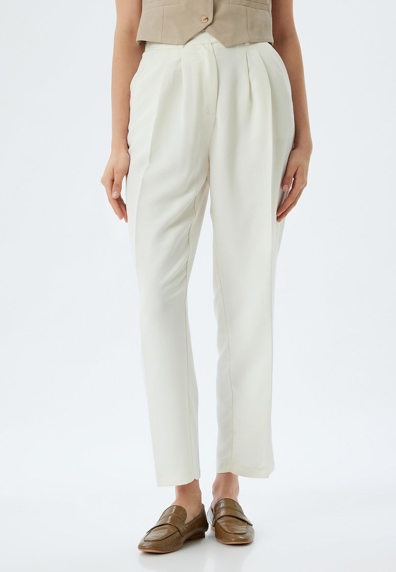 Pantaloni bianchi sartoriali con pieghe, realizzati in un tessuto liscio. Caratterizzati da una gamba dritta e abbinati a mocassini marroni.