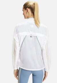 Lichte witte windjack met een mesh achterkant, grijze accenten, een trekkoord bij de hals en een opvallende logodetail op de bovenrug.