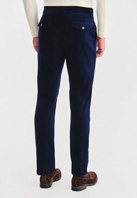 Granatowe spodnie corduroy o dopasowanym kroju, z dwiema tylnymi kieszeniami i gładką fakturą, w połączeniu z brązowymi zamszowymi butami.