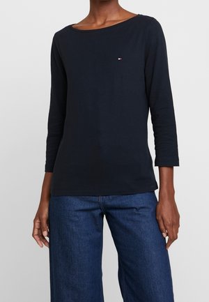 Langsleeve marineblauwe top van zacht katoen met een ronde hals en een klein logo op de borst, gecombineerd met wijdwijdte denim jeans.