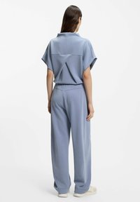Two-piece outfit in soft blue fabric; loose-fit short-sleeve top with unique back design and wide-leg pants, both with minimalist style.