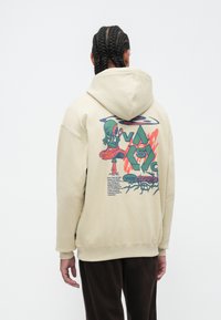 Beige hoodie met een kleurrijke grafische print op de achterkant, voorzien van illustraties, tekst, een ruime capuchon en ribgebreide manchetten.