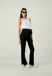 Tenue de grossesse avec un haut ajusté noir et blanc et un pantalon noir évasé. Des baskets blanches complètent le look. Tissu lisse, design épuré.