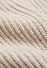 Gros plan sur un tissu en laine tricotée beige doux avec un motif côtelé diagonal et une texture duveteuse.