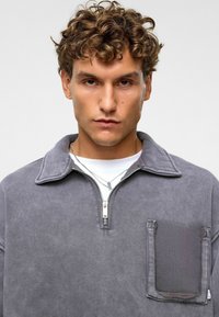 Grijze katoenen kwart-zip pullover met een kraag, voorzien van een voorzak met flap en zilveren ritsdetails. Glad textuur, casual ontwerp.