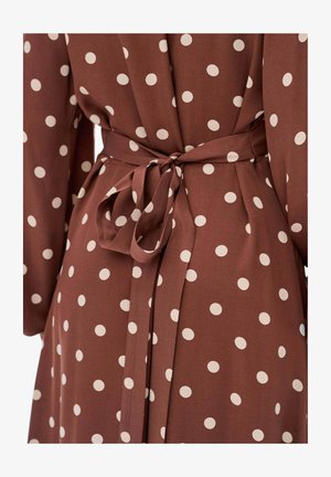 Brązowa sukienka z dużymi kremowymi kropkami, z długimi rękawami i wiązanym w pasie, wykonana z lekkiego materiału o gładkiej strukturze.