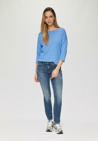 Hellblaues Langarmoberteil mit rundem Ausschnitt; kombiniert mit figurbetonten blauen Jeans und silbernen Sneakers. Einfaches Design, glatte Stoffstruktur.