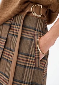 Bruine geruite rok met een beige neplederen riem, featuring een grote gouden gesp en zijzak, benadrukt met contrasterende strepen.