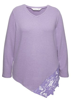 Vaaleanlila pitkähiha, jossa on V-pääntie, epäsymmetrinen helma ja pitsikoristelu yhdellä puolella. Pehmeä rakenne, minimalistinen muotoilu.