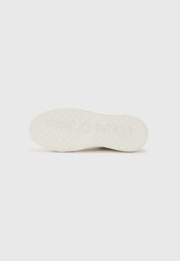Semelle de sneaker blanche avec un motif de grip texturé, présentant un logo embossé sur le caoutchouc et un design de bord lisse.