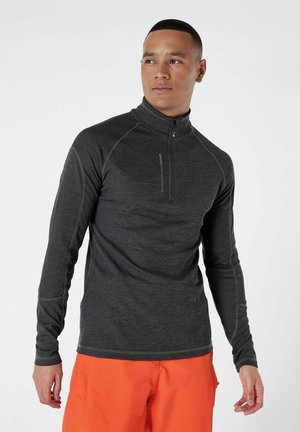 Maglia nera a maniche lunghe con zip al collo, con una finitura testurizzata e cuciture a contrasto; indossata con pantaloni corti arancioni, dal taglio aderente.