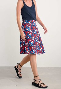 Jupe à motifs rouge, blanc et bleu mettant en avant des formes géométriques, avec une coupe évasée. Associée à des sandales noires à lanières et un débardeur marine.