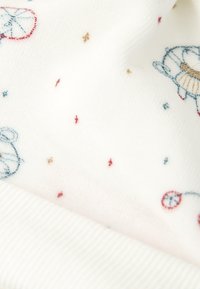 Tejido blanco con pequeños diseños bordados de temática marina, que incluyen tortugas azules y puntos rojos, azules y marrones esparcidos por toda la tela.
