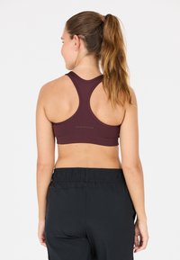 Bordeaux sportbh med racerback-design, tillverkad av stretchigt tyg. Ena sidan har "ENDURANCE"-logotypen; matchas med svarta träningsbyxor.