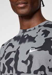 Hallide kamuflaažiga lühikeste varrukatega särk, mis on valmistatud hingavast kangast; esiosas on valge Nike'i logo ja ümmargune kaelus.