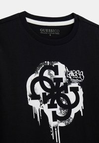 Maglietta nera in cotone biologico, con un audace design grafico bianco caratterizzato da lettere sovrapposte e dettagli di gocce di vernice spray.