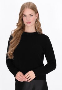 Maglione nero, materiale lavorato a maglia, scollatura rotonda, maniche lunghe, corpetto aderente, polsini e orlo a costine, indossato sopra una gonna nera di seta.