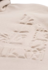 Tessuto beige con un motivo testurizzato caratterizzato da elementi in rilievo. Texture liscia e aspetto morbido, ideale per abbigliamento casual.