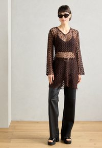 Brown lace overlay top with long sleeves, V-neck, and sheer sections, paired with black leather trousers and chunky heeled sandals.