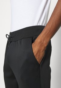 Pantaloni jogger neri realizzati in tessuto morbido, con vita elastica e cordino e tasche laterali.