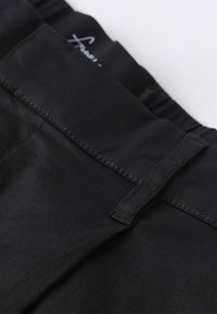 Pantalons noirs avec une texture lisse, présentant une taille large et des détails cousus. Le tissu semble extensible et durable.