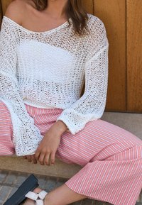 Haut blanc en maille avec manches longues évasées, associé à un pantalon ample à larges rayures roses. Le haut présente une maille lâche et ouverte avec une finition texturée.