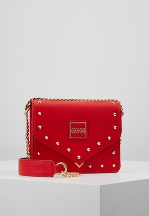 Bolso sintético rojo con tachuelas doradas, diseño acolchado y una correa de cadena. Incluye una placa con el logo y una correa de muñeca desmontable.