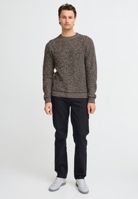 Brown knit sweater with a textured pattern, round neckline, and ribbed cuffs. Paired with black pants and gray sneakers.